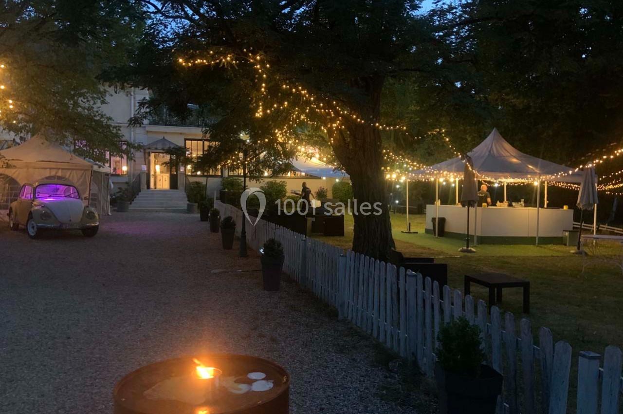 Jardin éclairé en soirée avec guirlandes lumineuses, tentes blanches et une voiture ancienne stationnée.