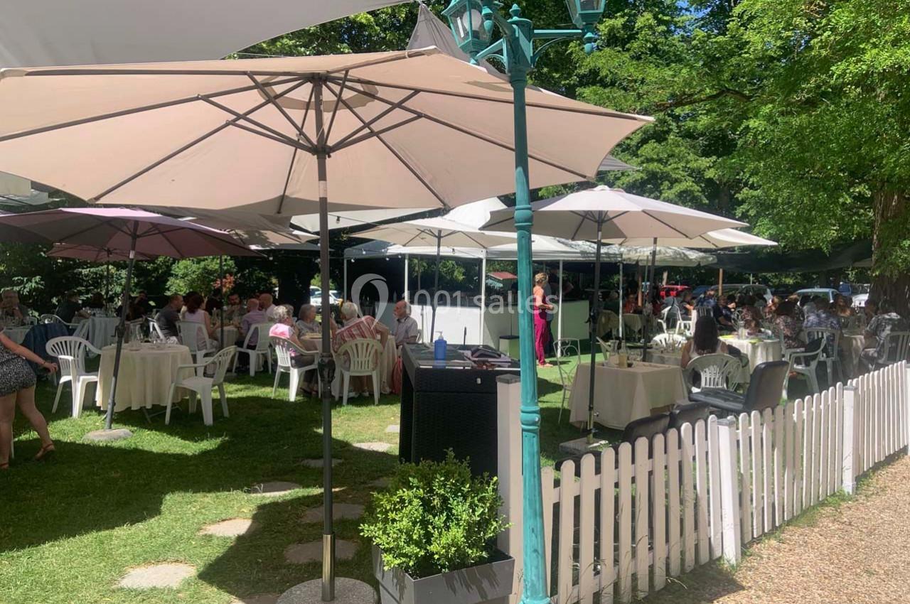 Terrasse extérieure d'un restaurant avec des tables sous des parasols, entourée d'arbres et d'une clôture blanche.