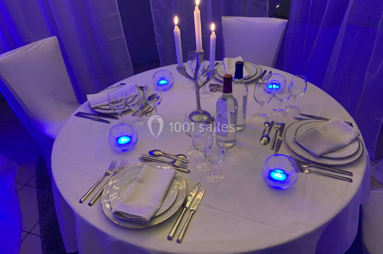 Table ronde élégamment dressée avec nappes blanches, chandeliers allumés et vaisselle raffinée dans une ambiance lumineuse…