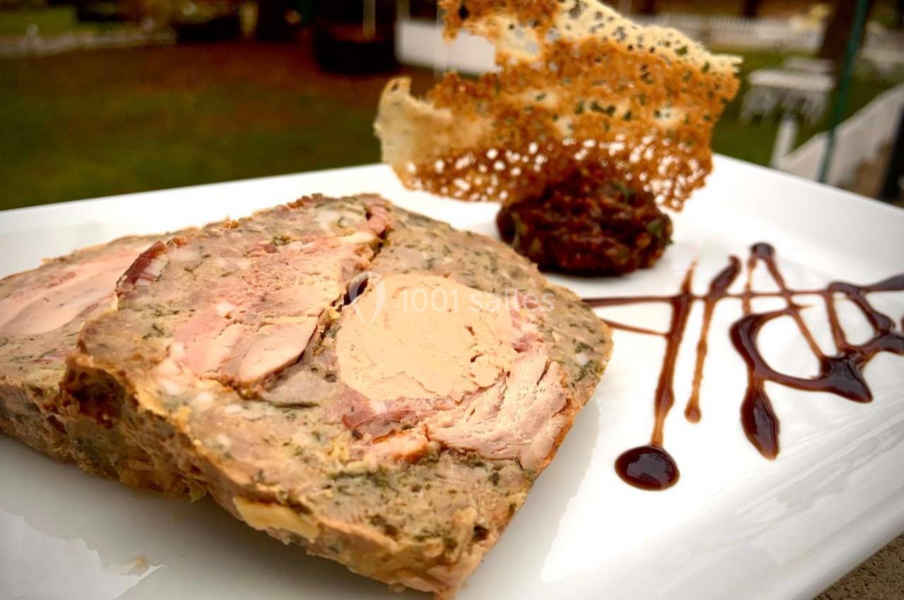 Terrine de viande garnie de foie gras, accompagnée de sauce balsamique, d'une tuile croustillante et d'une garniture.