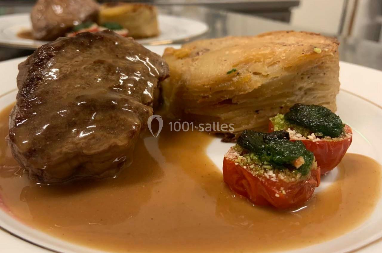 Assiette contenant un morceau de viande nappé de sauce, un gratin de pommes de terre et des tomates cerises garnies.