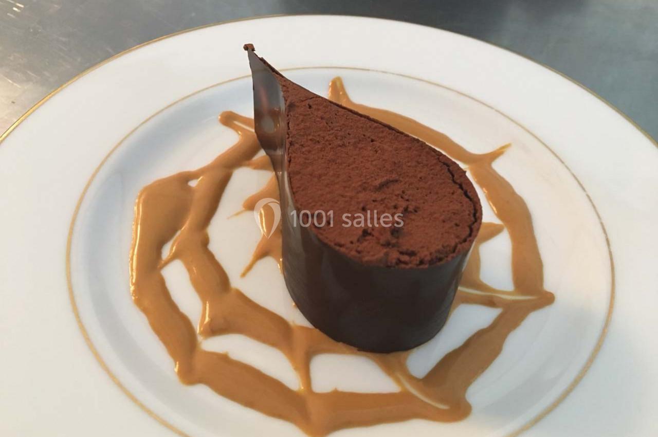 Dessert au chocolat en forme de goutte, entouré d'un décor de sauce caramel sur une assiette blanche.