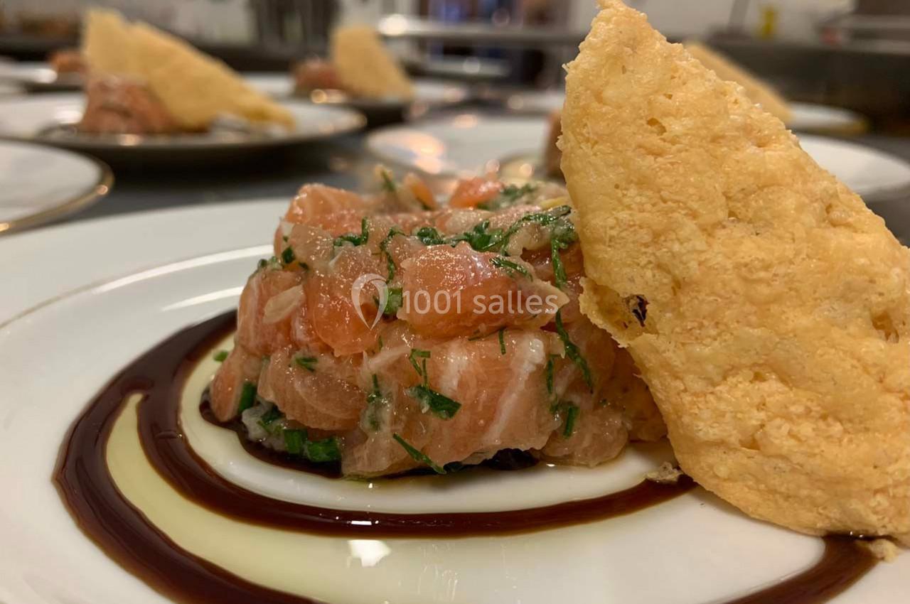 Tartare de saumon frais avec herbes, dressé sur une assiette avec un filet de sauce et une tuile croustillante.