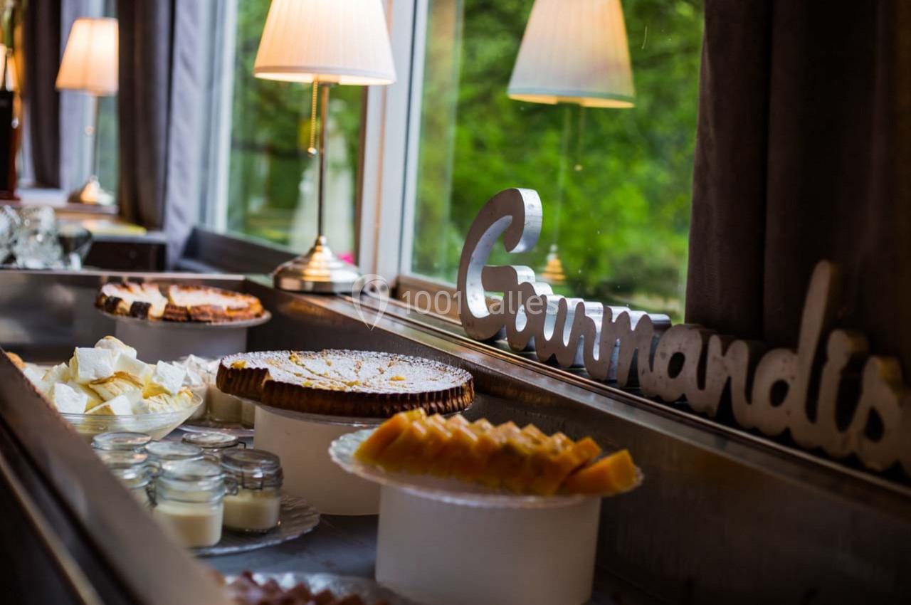 Buffet avec desserts variés, incluant tarte, fromage, verrines et décoration lumineuse près d'une fenêtre.