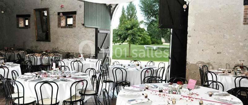 Salle de réception avec tables rondes dressées, chaises noires et vue sur un jardin verdoyant à travers une grande ouverture.