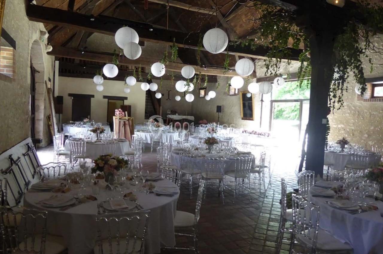 Salle de réception rustique décorée de lanternes blanches suspendues et de tables dressées pour un événement.