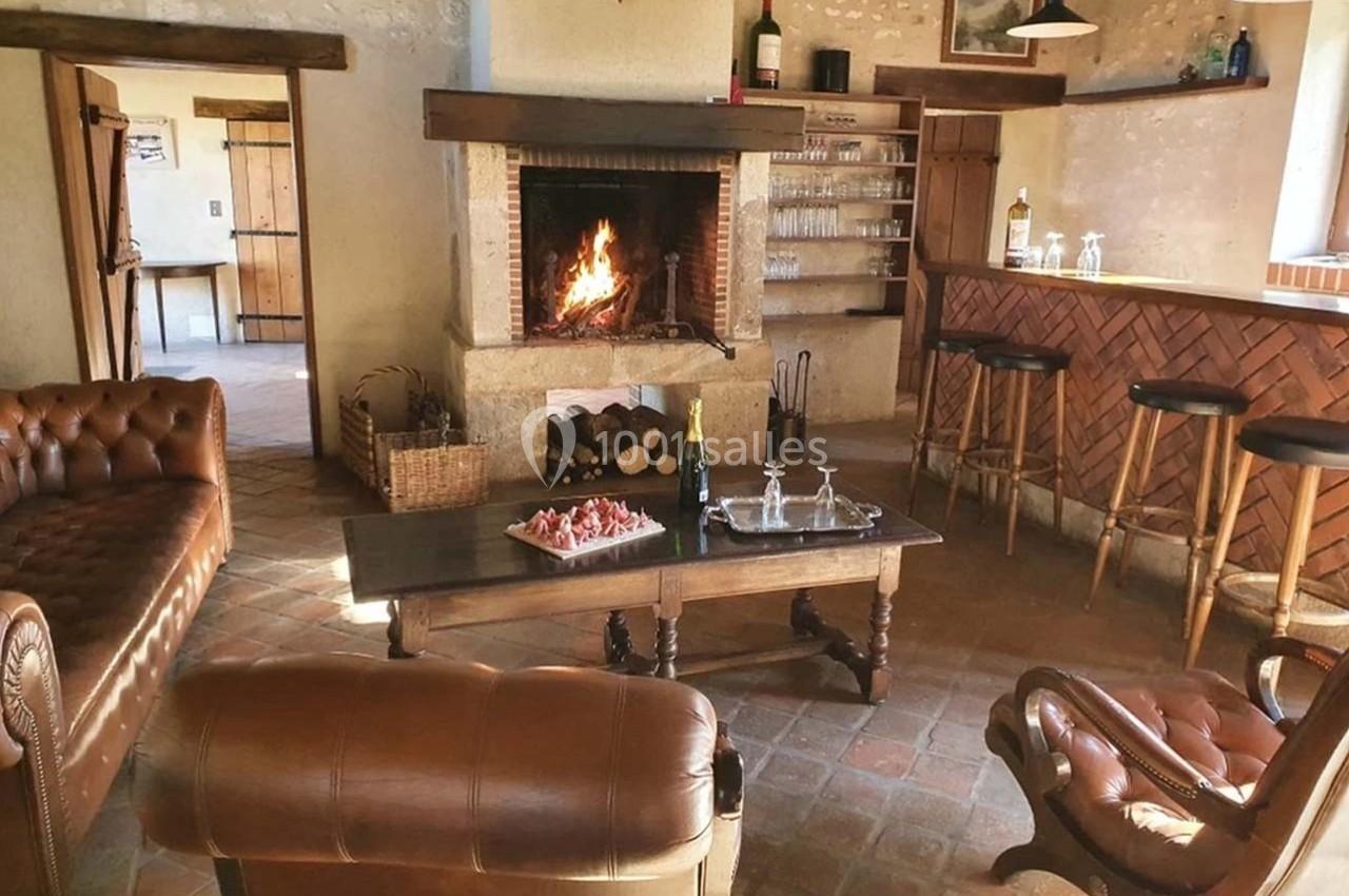 Salle chaleureuse avec cheminée allumée, canapé en cuir, table basse et bar en bois dans un décor rustique.