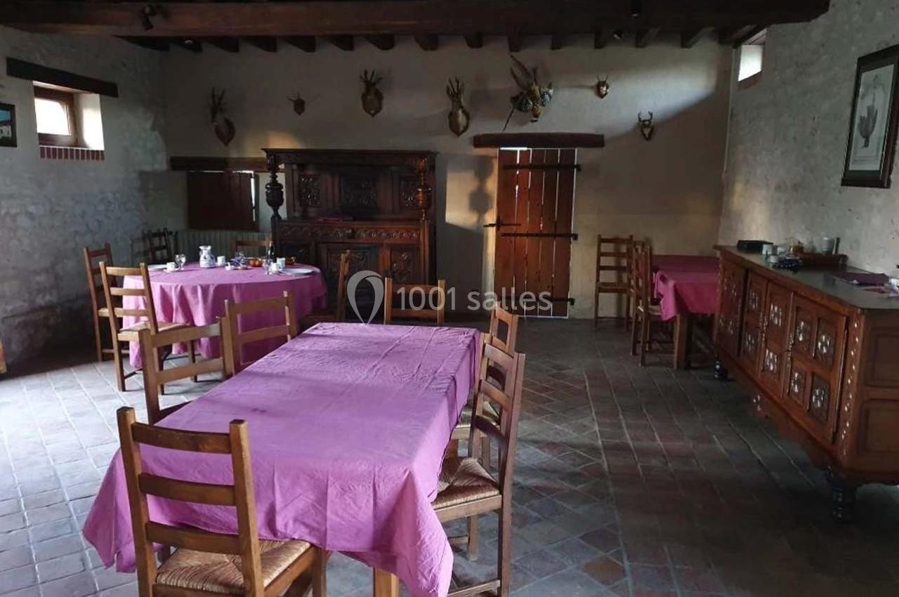 Salle à manger rustique avec tables recouvertes de nappes violettes, meubles en bois et décoration murale avec trophées.