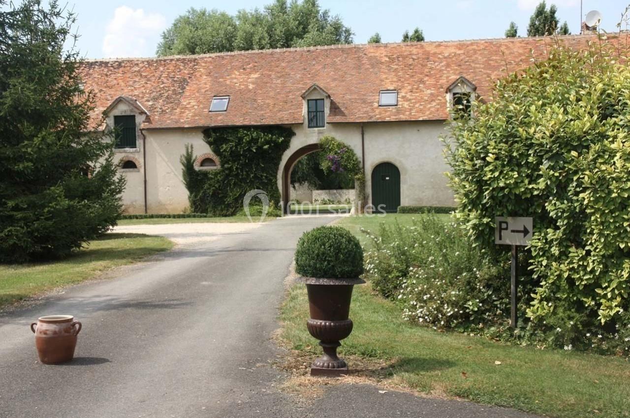 Allée menant à un bâtiment en pierre avec toit en tuiles, entouré de végétation et d'un panneau indiquant un parking.