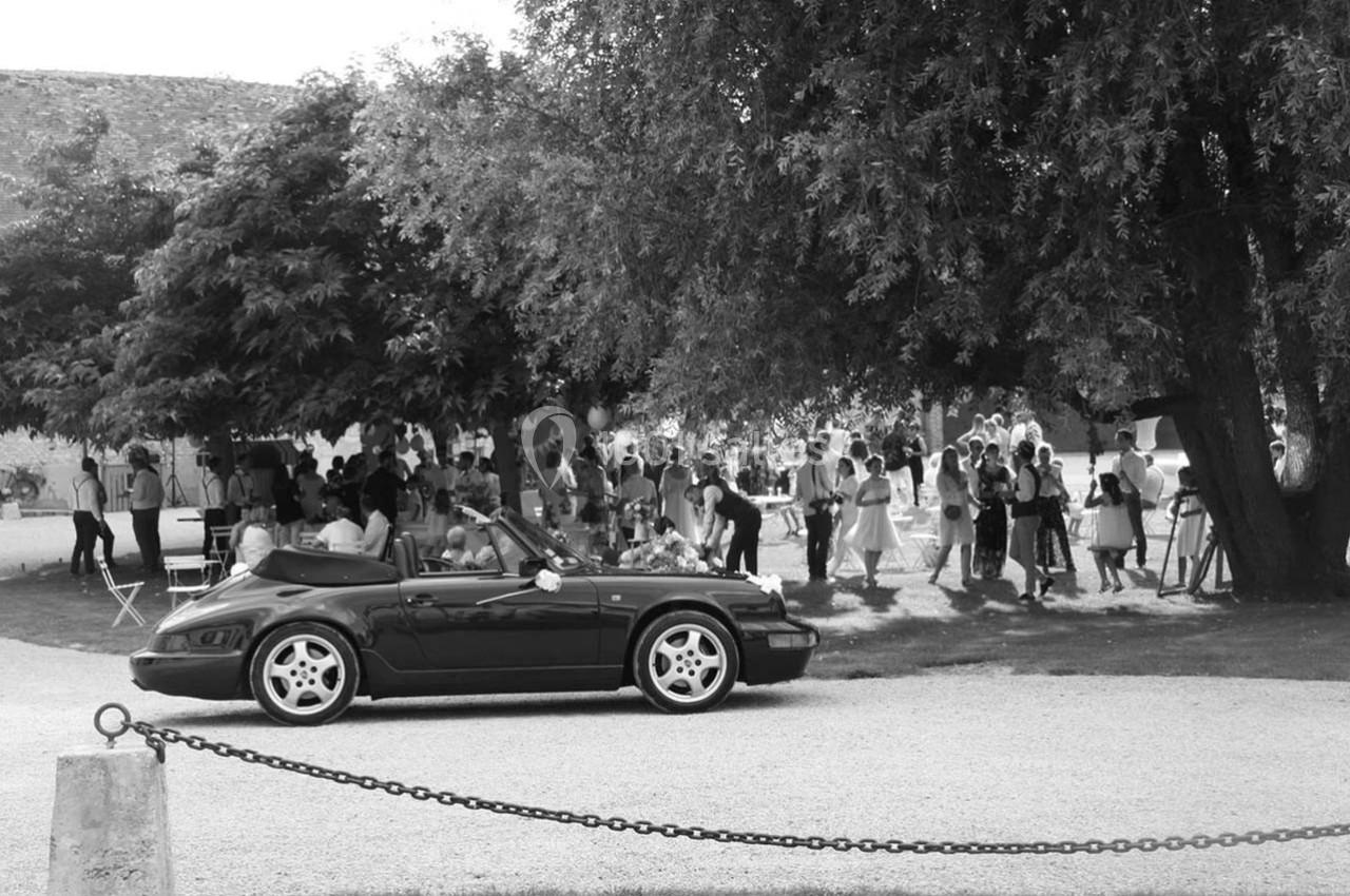 Voiture décapotable noire garée devant un groupe de personnes rassemblées sous des arbres dans un espace extérieur.