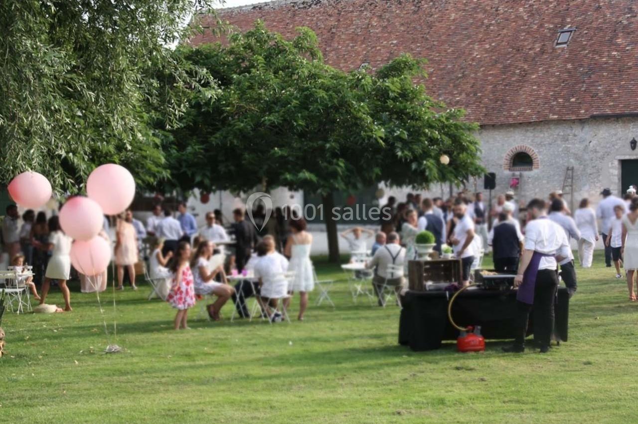 Groupe de personnes rassemblées dans un jardin pour un événement, avec des ballons roses et des tables installées.