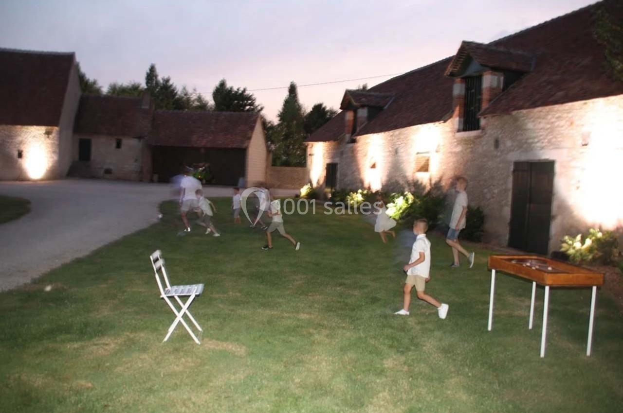 Des enfants jouent sur une pelouse au crépuscule devant des bâtiments en pierre éclairés.