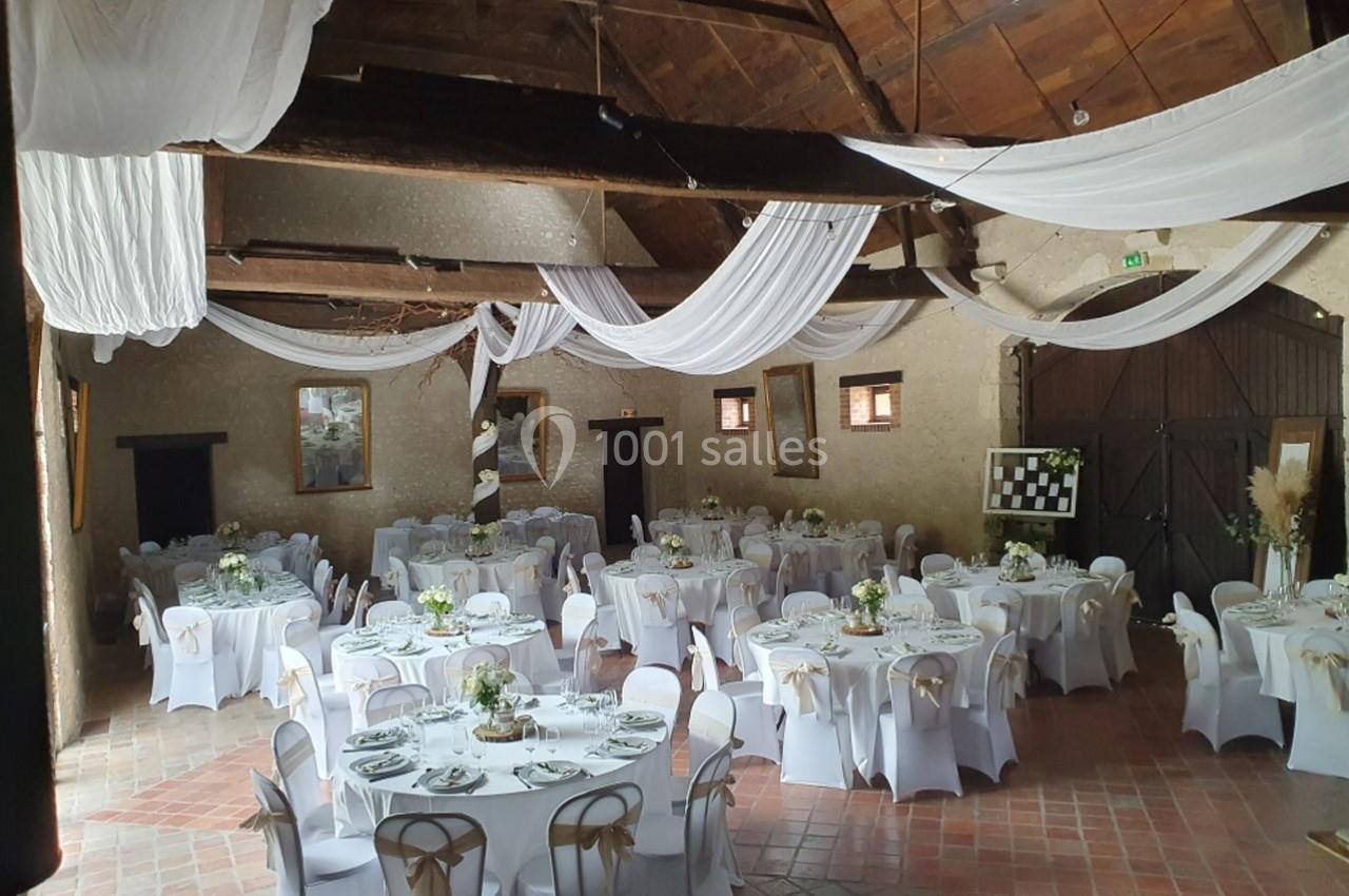 Salle de réception avec tables rondes décorées, nappes blanches et plafonds ornés de voilages suspendus.