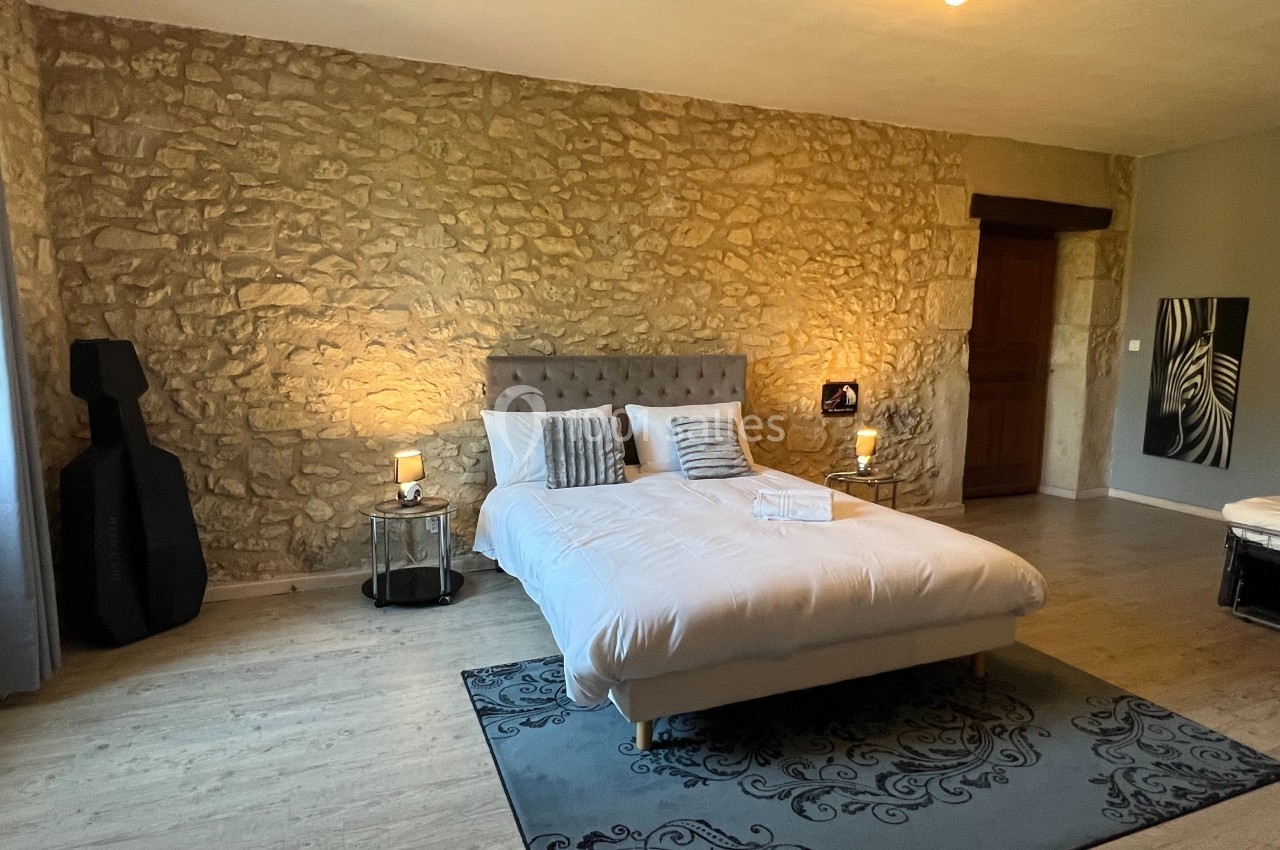 Chambre avec mur en pierre, lit double, lampes de chevet allumées et décoration moderne sur un sol en parquet.