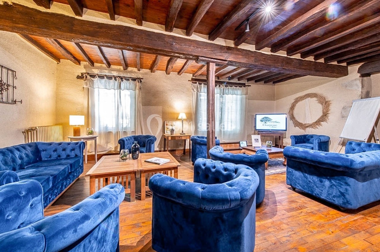 Salon chaleureux avec fauteuils bleus en velours, table basse en bois, poutres apparentes et lumière naturelle.