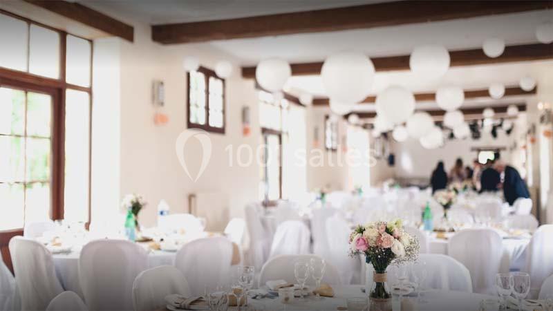 Salle de réception lumineuse décorée de lanternes blanches suspendues et de tables avec nappes blanches et bouquets de…