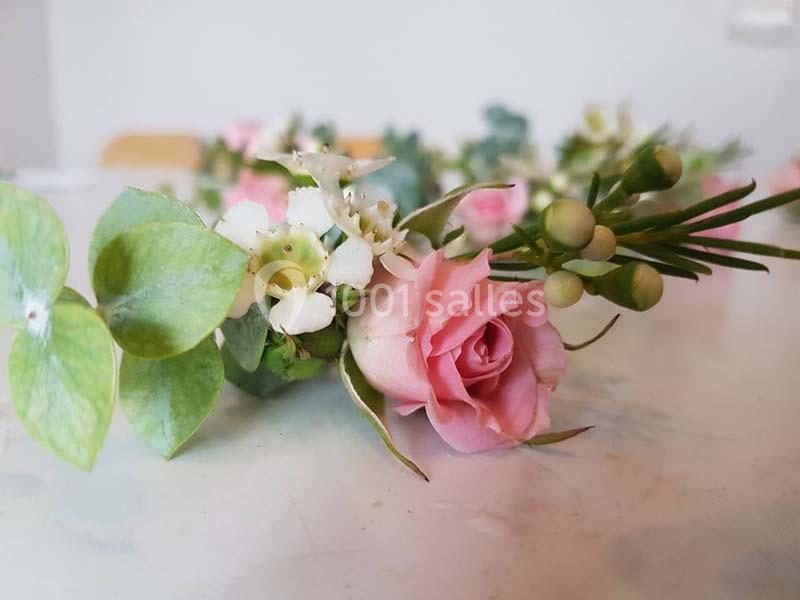 Branche de fleurs composée de roses roses, de feuillage vert et de petites fleurs blanches sur une table.