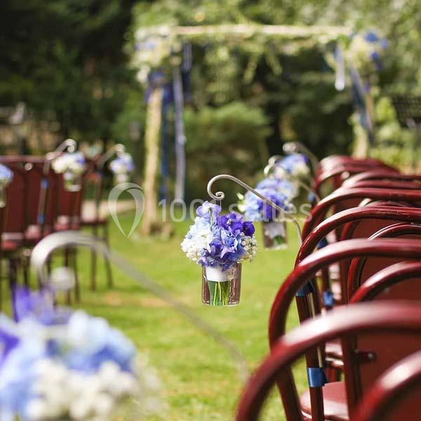 Chaises rouges alignées en extérieur avec des bouquets de fleurs bleues suspendus, sous une arche décorée.