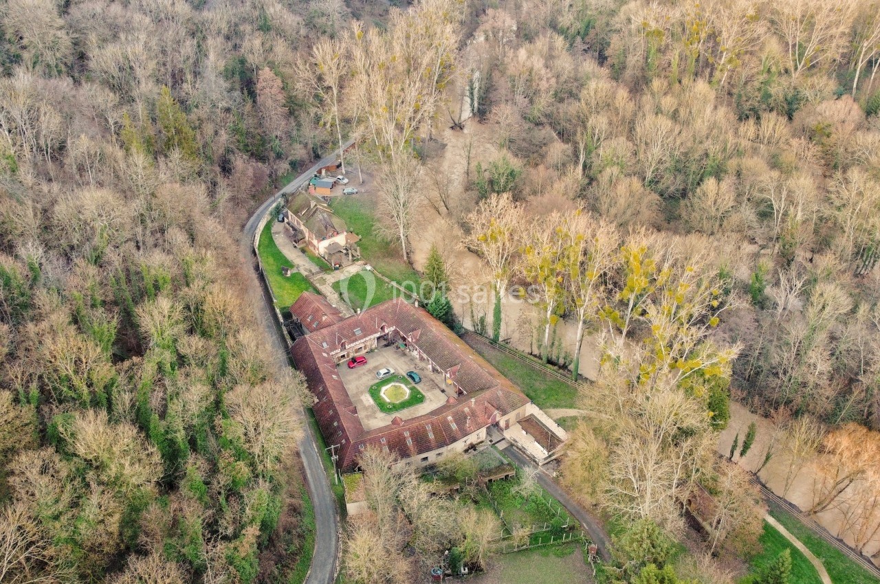 Vue aérienne d'un domaine entouré de forêt, avec bâtiments en briques rouges, cour centrale et routes sinueuses.