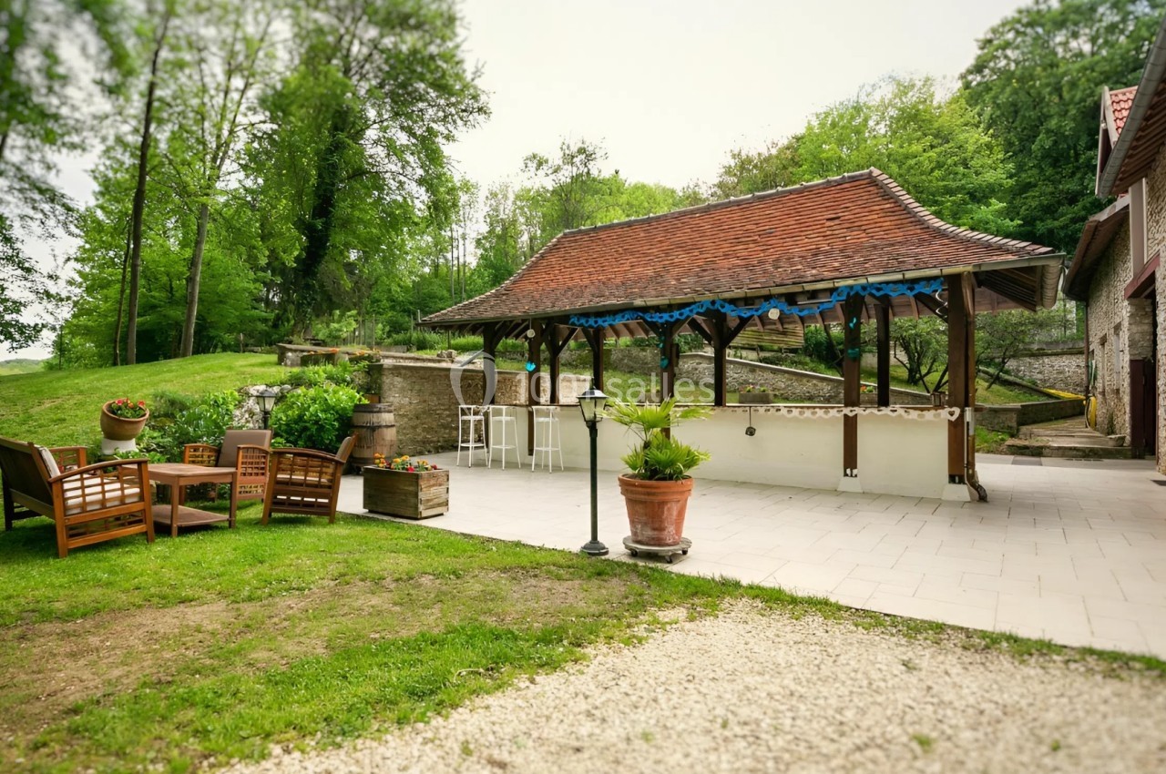 Espace extérieur avec terrasse pavée, pergola en bois, mobilier de jardin et verdure environnante.
