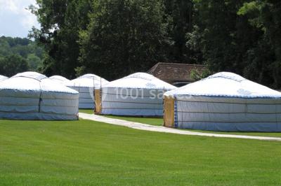 Intérieur d'une yourte avec trois lits en bois sculpté disposés autour d'un espace central sur un sol en bois.