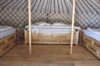 Intérieur d'une yourte avec trois lits en bois sculpté disposés autour d'un espace central sur un sol en bois.