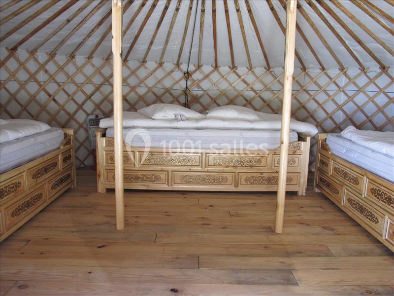 Intérieur d'une yourte avec trois lits en bois sculpté disposés autour d'un espace central sur un sol en bois.