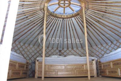 Intérieur d'une yourte avec trois lits en bois sculpté disposés autour d'un espace central sur un sol en bois.