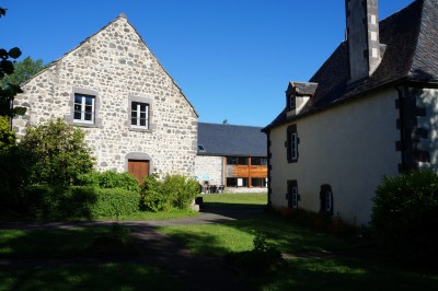 Deux barbecues modernes en métal noir avec plans de travail en bois, installés devant un bâtiment en pierre.