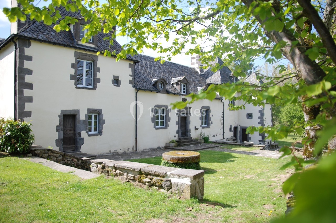 Façade d'une maison en pierre de style traditionnel entourée de verdure et éclairée par une lumière naturelle.