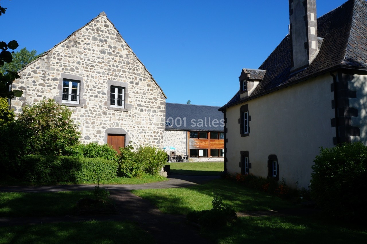 Deux bâtiments en pierre avec jardin verdoyant sous un ciel bleu clair.