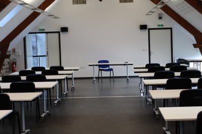 Salle de réunion équipée de chaises rouges et noires, d'un vidéoprojecteur et d'un écran blanc.