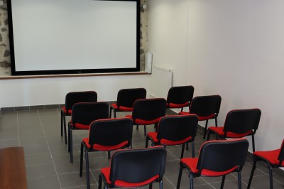 Salle de réunion équipée de chaises rouges et noires, d'un vidéoprojecteur et d'un écran blanc.