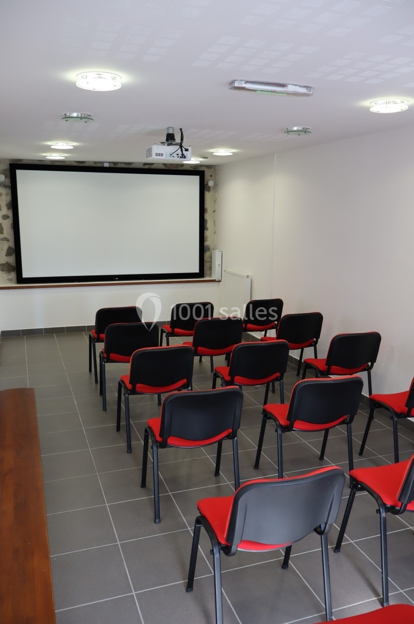Salle de réunion équipée de chaises rouges et noires, d'un vidéoprojecteur et d'un écran blanc.