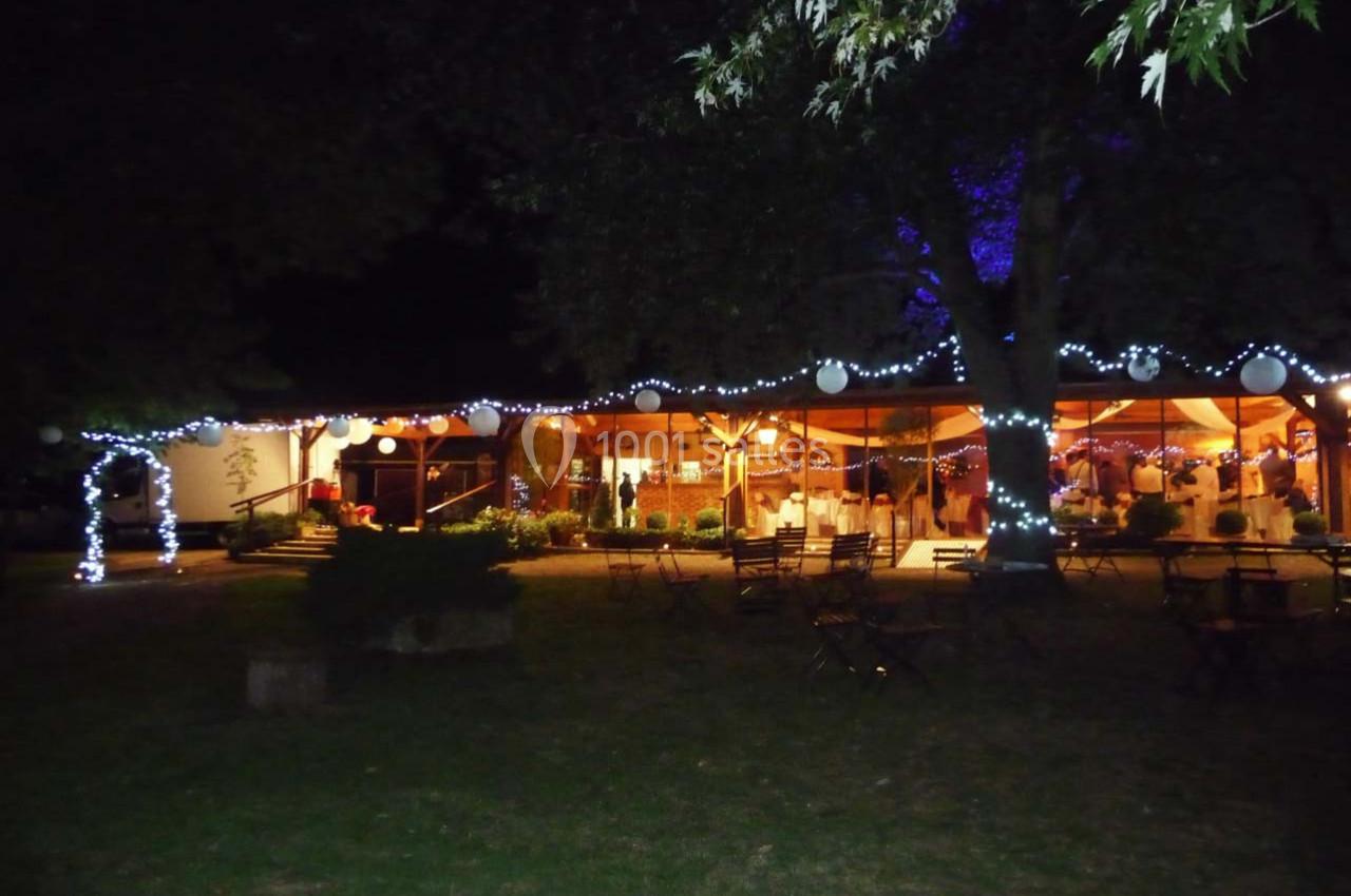 Salle éclairée en soirée avec des guirlandes lumineuses et des tables disposées dans un jardin sombre.