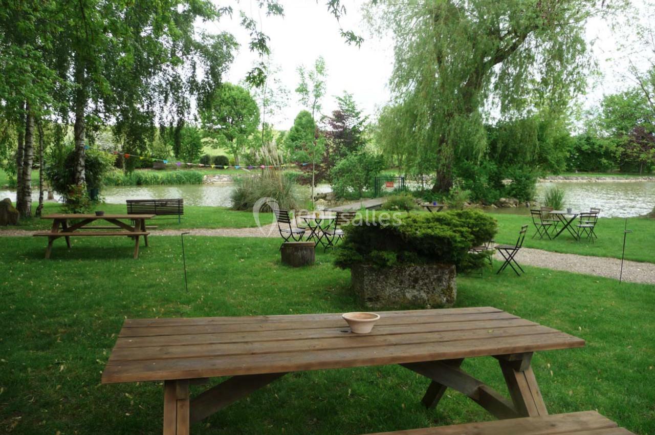 Table de pique-nique en bois sur une pelouse verdoyante, entourée d'arbres et proche d'un étang paisible.