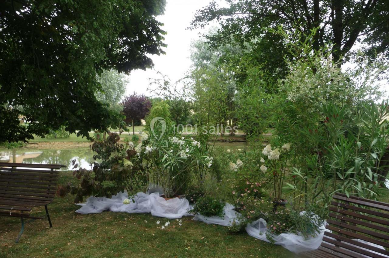 Des plantes et arbustes disposés sur une pelouse près d'un étang, entourés d'arbres et de bancs en bois.