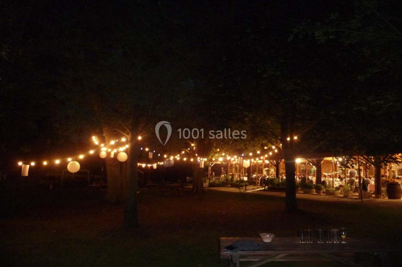 Guirlandes lumineuses suspendues dans un jardin sombre, éclairant des tables et une structure en arrière-plan.