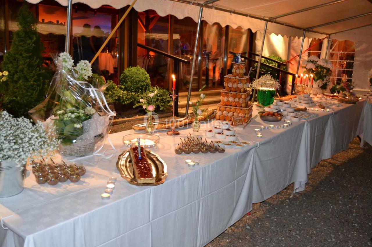 Buffet de desserts dressé sous une tente, avec pièces montées, bougies et décorations végétales.
