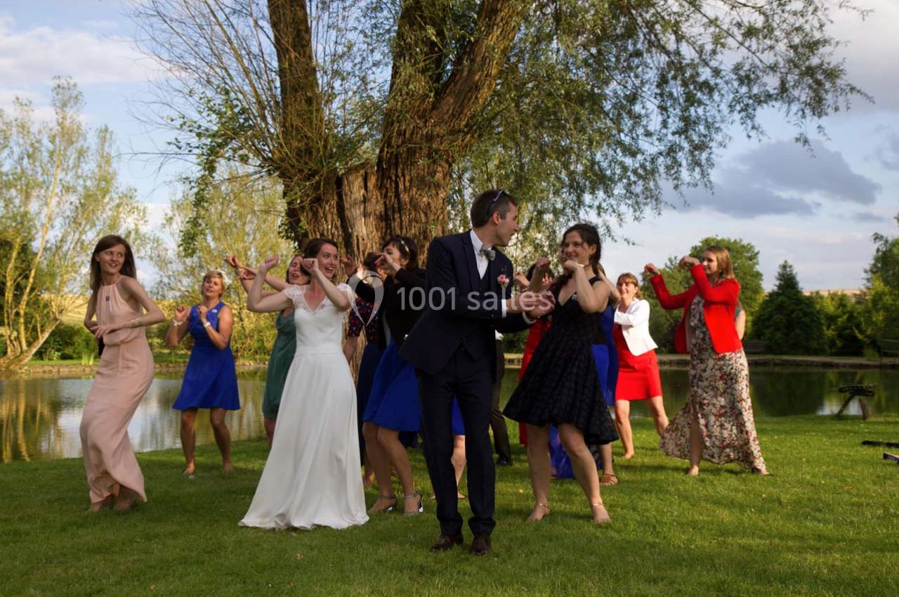 Des invités dansent en plein air près d'un arbre et d'un étang lors d'une célébration, avec une mariée au centre.