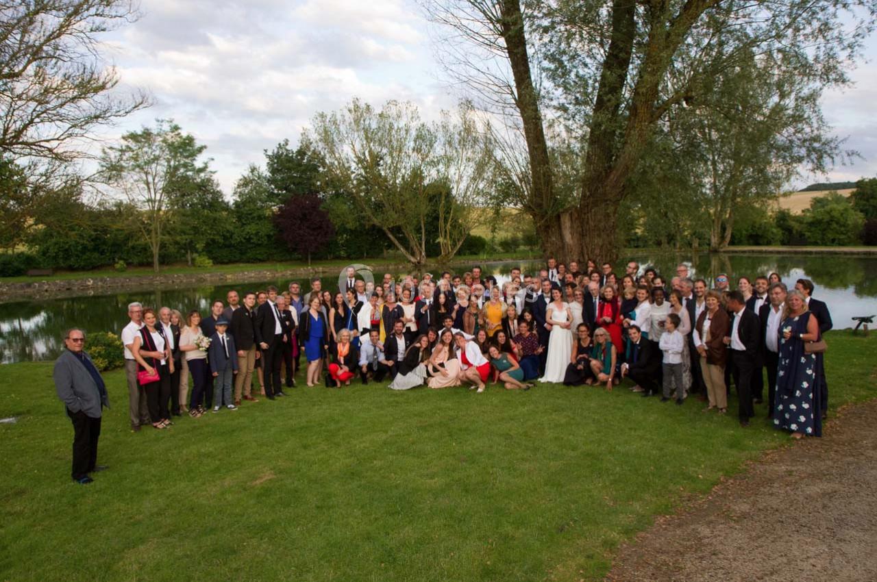 Groupe de personnes posant sur une pelouse près d'un étang, entouré d'arbres par temps clair.