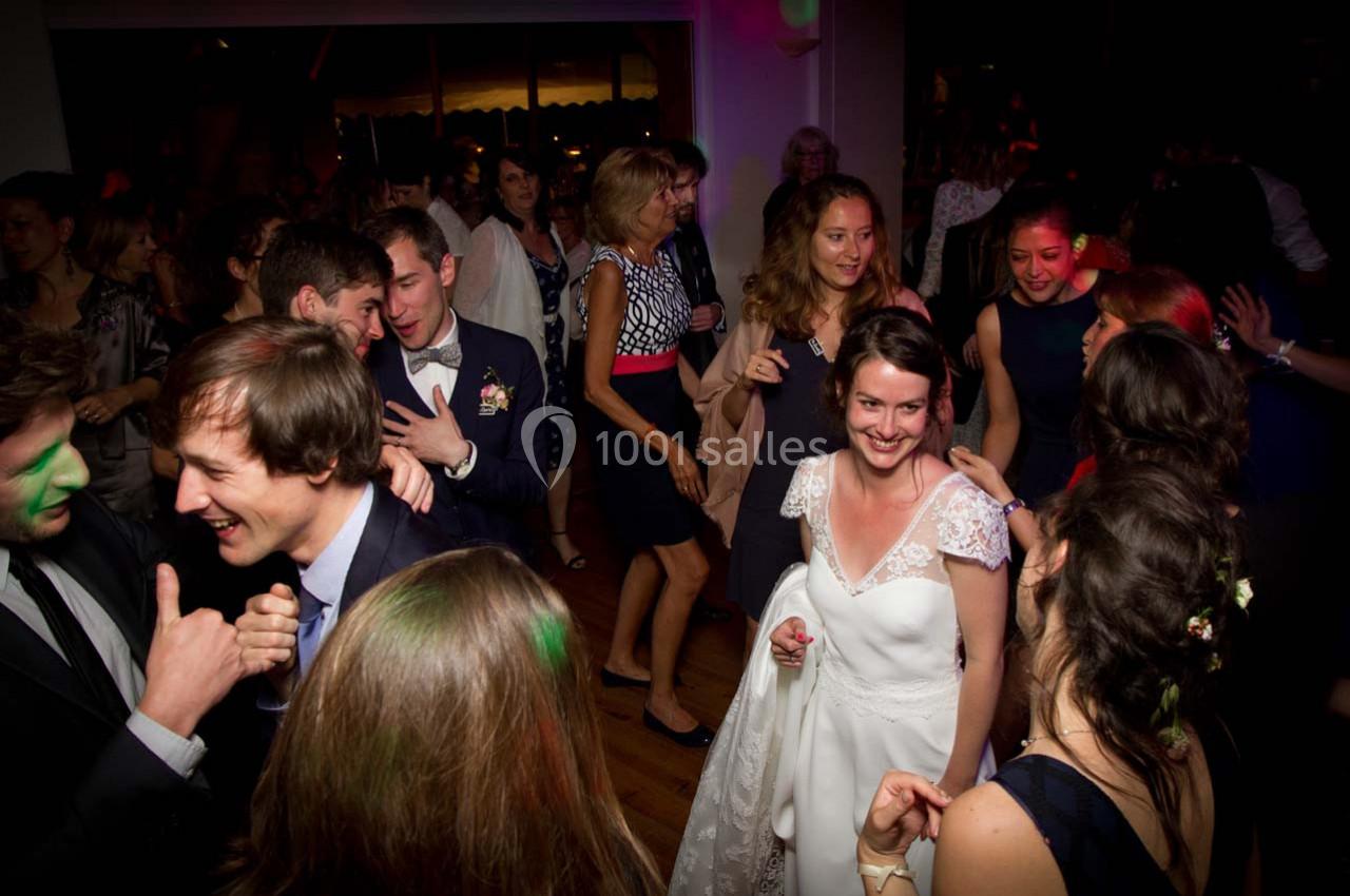 Des invités dansent et discutent lors d'une réception de mariage dans une salle faiblement éclairée.