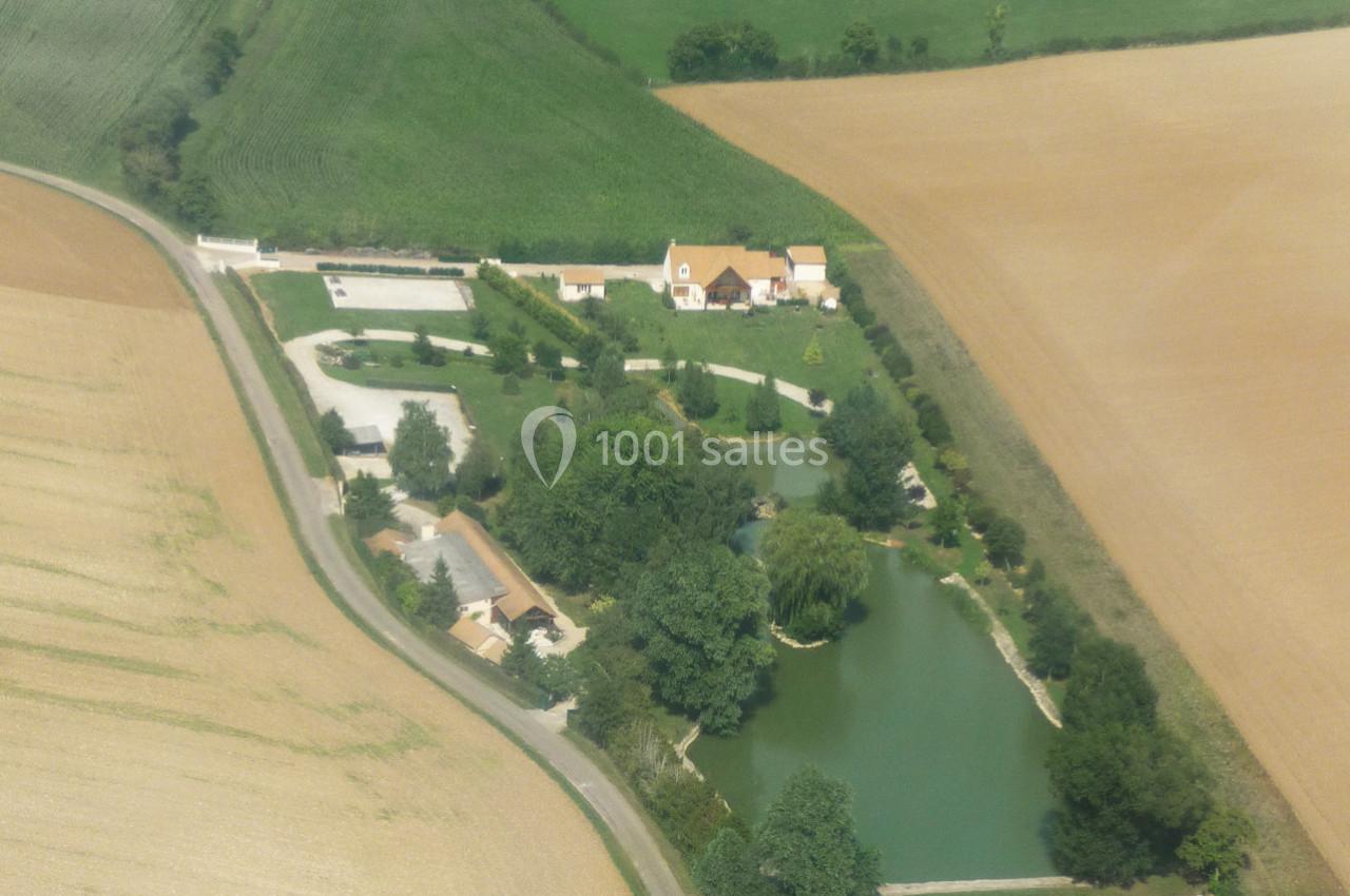 Vue aérienne d'une propriété rurale avec étang, arbres, bâtiments et champs environnants.