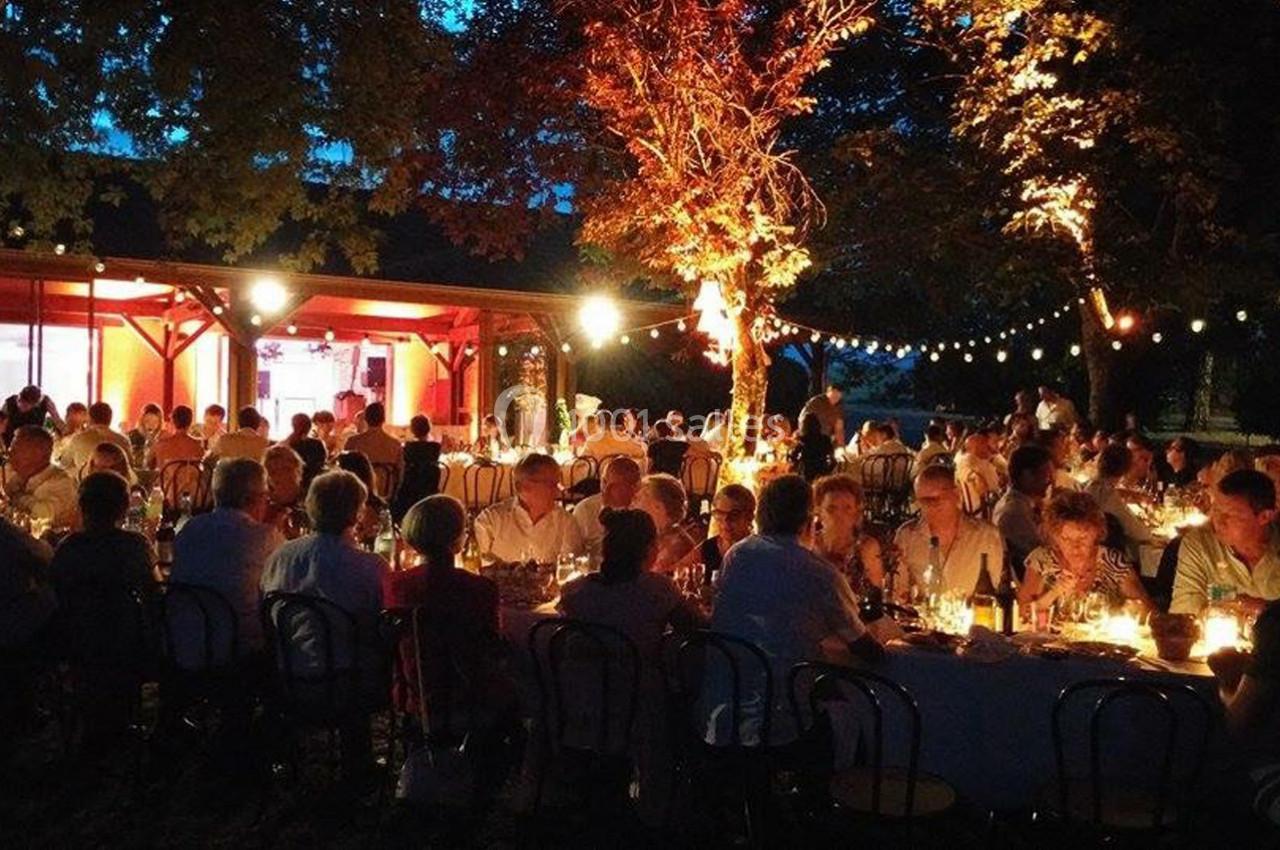 Groupe de personnes dînant en soirée dans un jardin éclairé par des guirlandes lumineuses et des lampes.