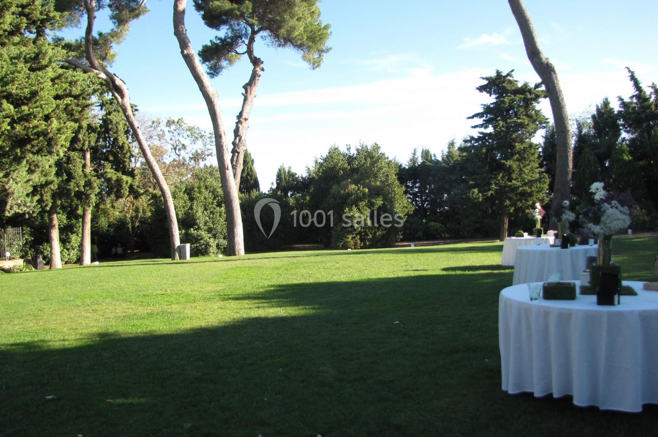 Location salle Pomérols (Hérault) - Domaine Fon de Rey #38 Pelouse verdoyante avec des tables rondes dressées en extérieur, entourée d'arbres et sous un ciel dégagé.