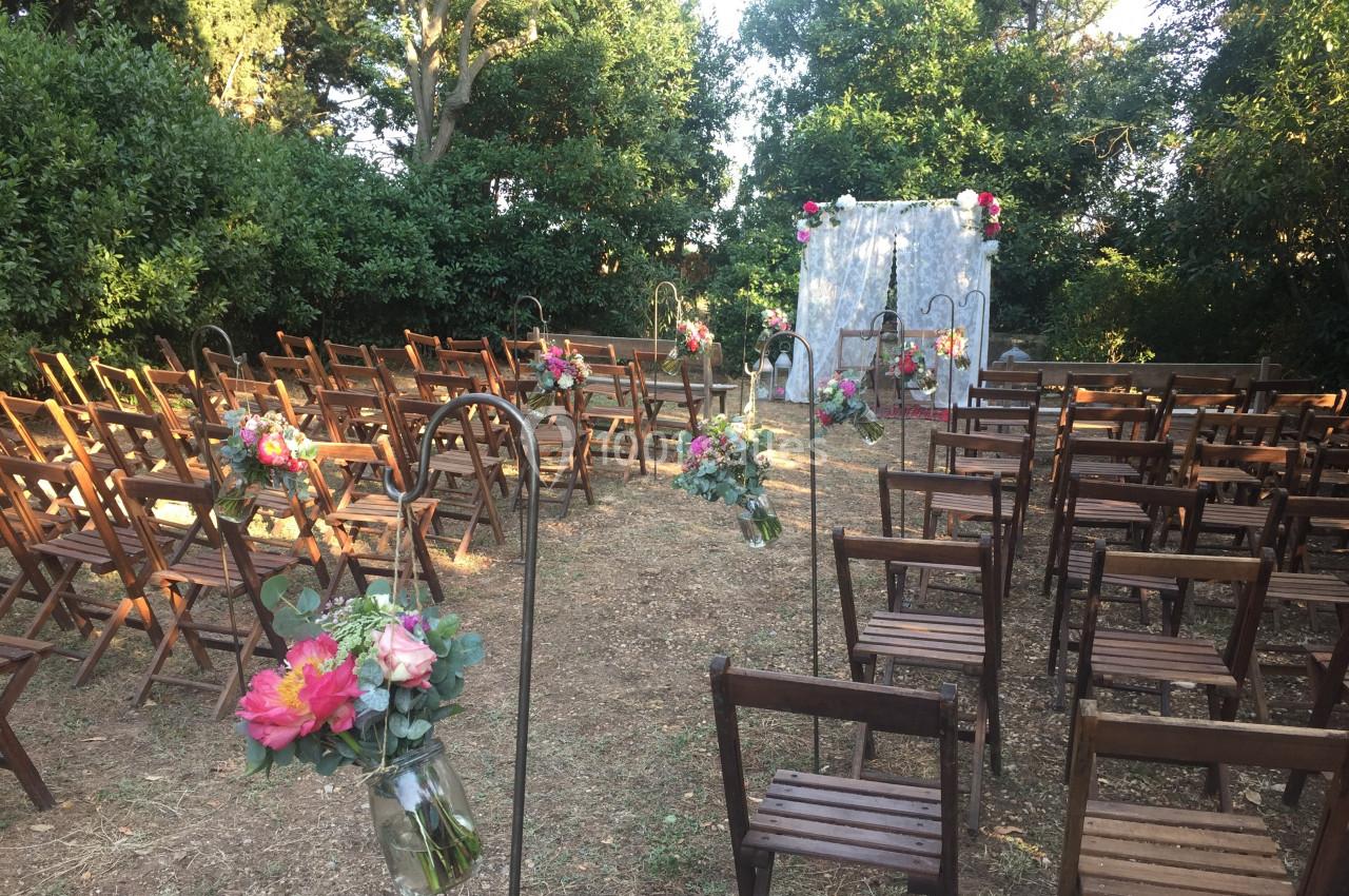Location salle Pomérols (Hérault) - Domaine Fon de Rey #58 Chaises en bois disposées en rangées dans un jardin, décorées de fleurs, face à une arche ornée pour une cérémonie.
