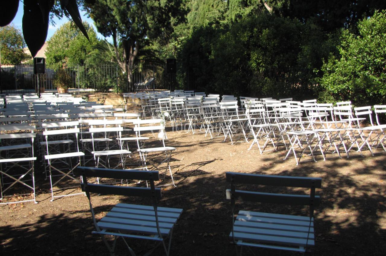 Location salle Pomérols (Hérault) - Domaine Fon de Rey #62 Chaises blanches pliantes disposées en rangées dans un espace extérieur entouré de végétation.