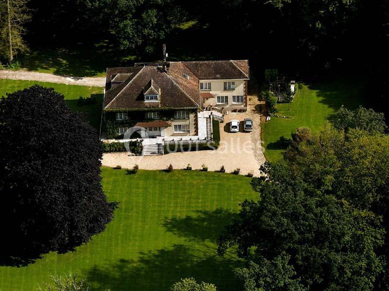Vue aérienne d'une grande maison entourée d'un jardin verdoyant avec une allée en gravier et des arbres matures.