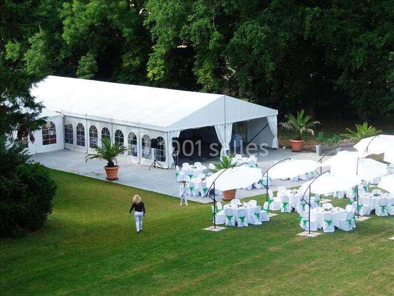 Grande tente blanche avec tables et chaises décorées sous des parasols, installées dans un jardin verdoyant.