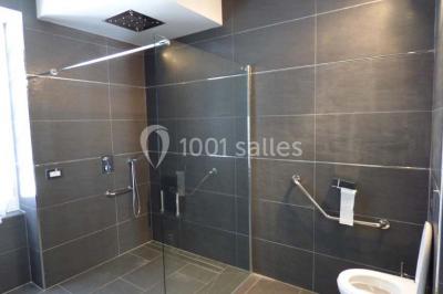 Salle de bain moderne avec douche à l'italienne, barres d'appui, toilettes et carrelage gris foncé.